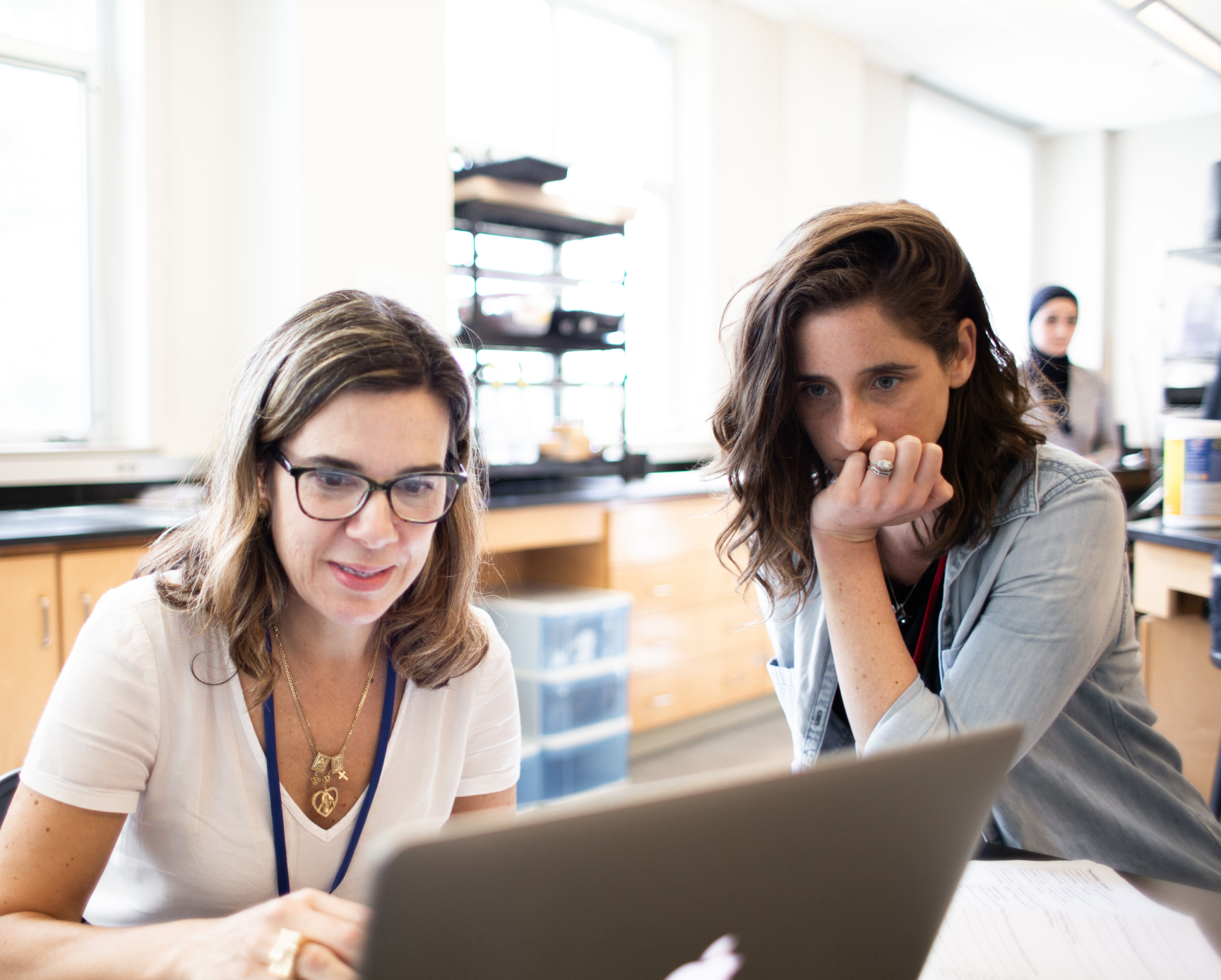Image of a woman at a laptop computer while another woman looks on.